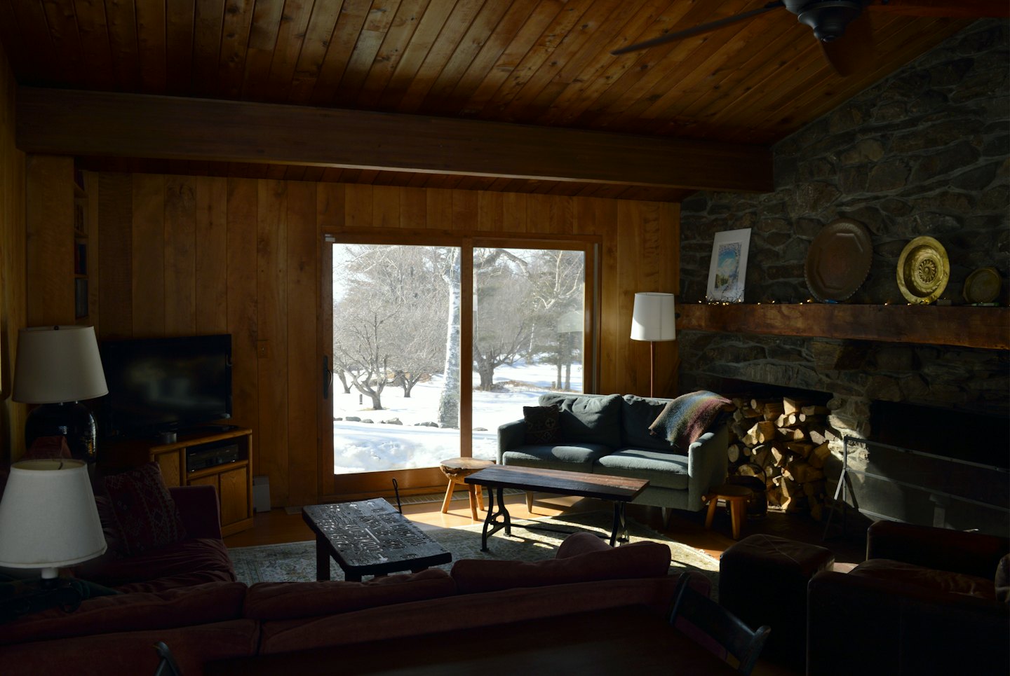 Gemütliches Wohnzimmer mit Steinkamin und Blick auf verschneiten Wald.