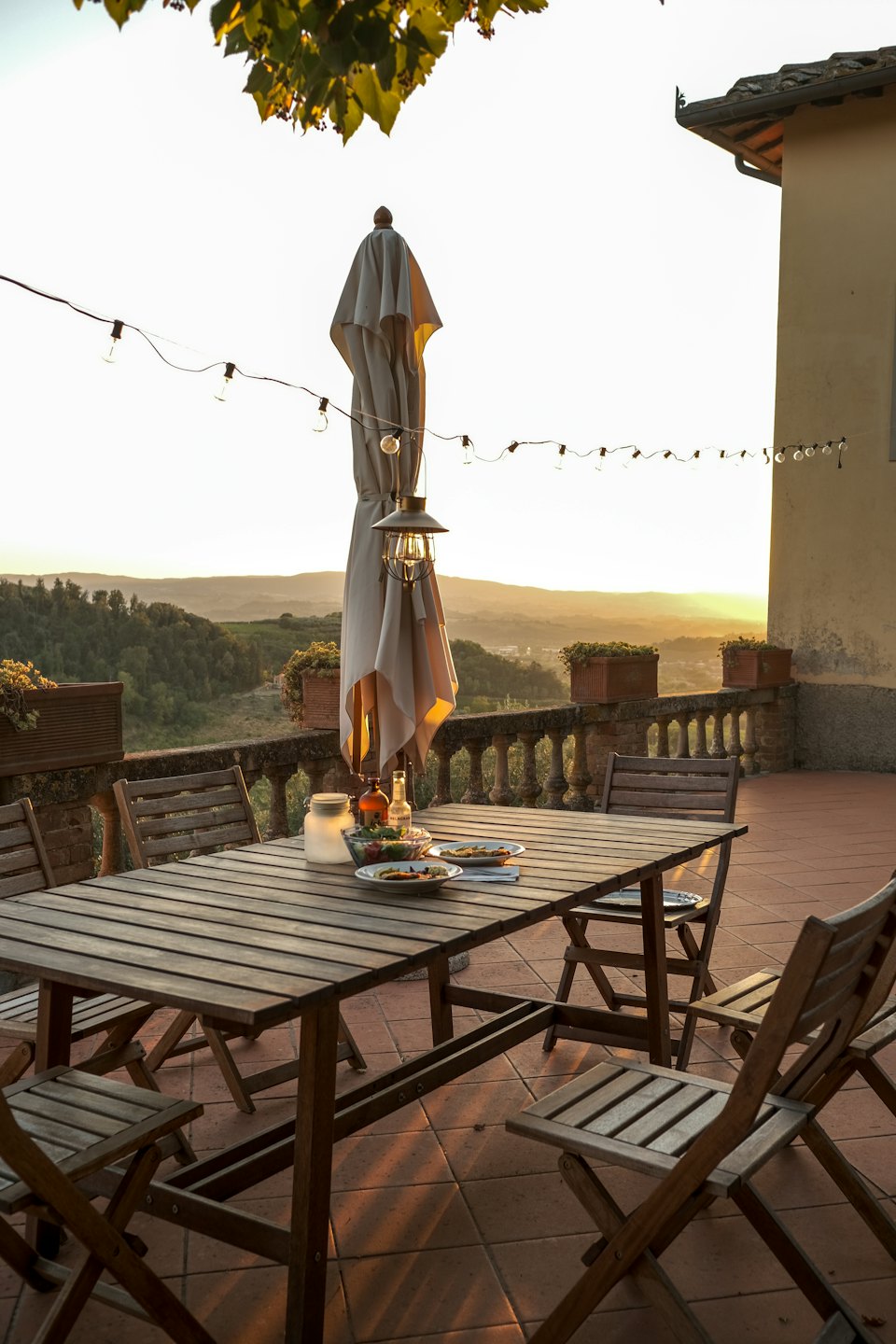 Terrassentisch im Freien mit Essen und Getränken und Blick auf die Hügel bei Sonnenuntergang.