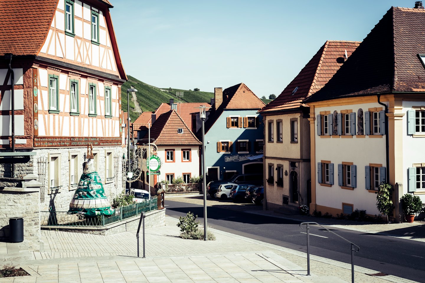 Traditionelle Häuser säumen eine Kopfsteinpflasterstraße, die zu grünen Weinbergen führt.