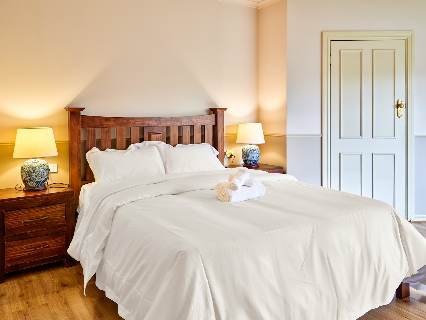 Ein gemachtes Bett mit Holz-Kopfteil und blauen Lampen.
